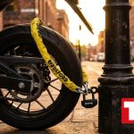 Moto asegurada con cadena antirrobo amarilla a un punto fijo en una calle al atardecer