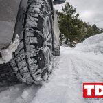 Rueda delantera de un coche con cadena de nieve metalica en una carretera de montana nevada