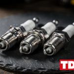 Tres bujias nuevas de distinta rosca y tamano sobre una superficie de pizarra