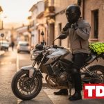 Motorista abrochandose el casco con guantes de proteccion y botas cerradas junto a su moto